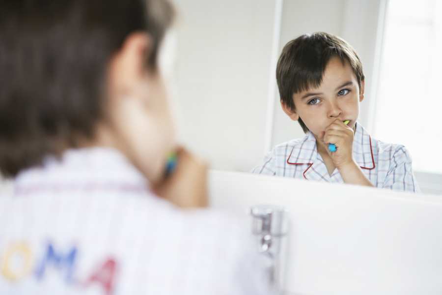 A young boy diligently brushing his teeth in front of a mirror, maintaining good oral hygiene habits