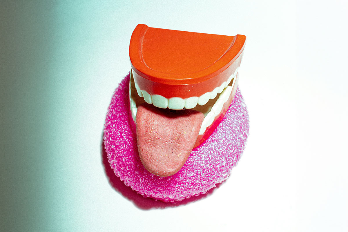 A plastic chattering teeth novelty toy with its tongue sticking out resting inside a bright pink mesh dish scrubber.