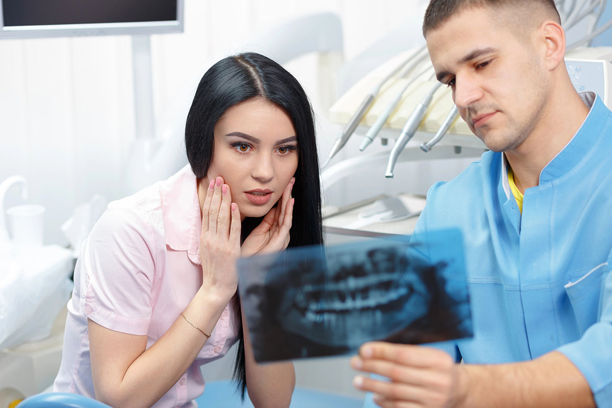 A male dentist showing a panoramic dental X-ray film to a concerned female patient in a clinical treatment room.