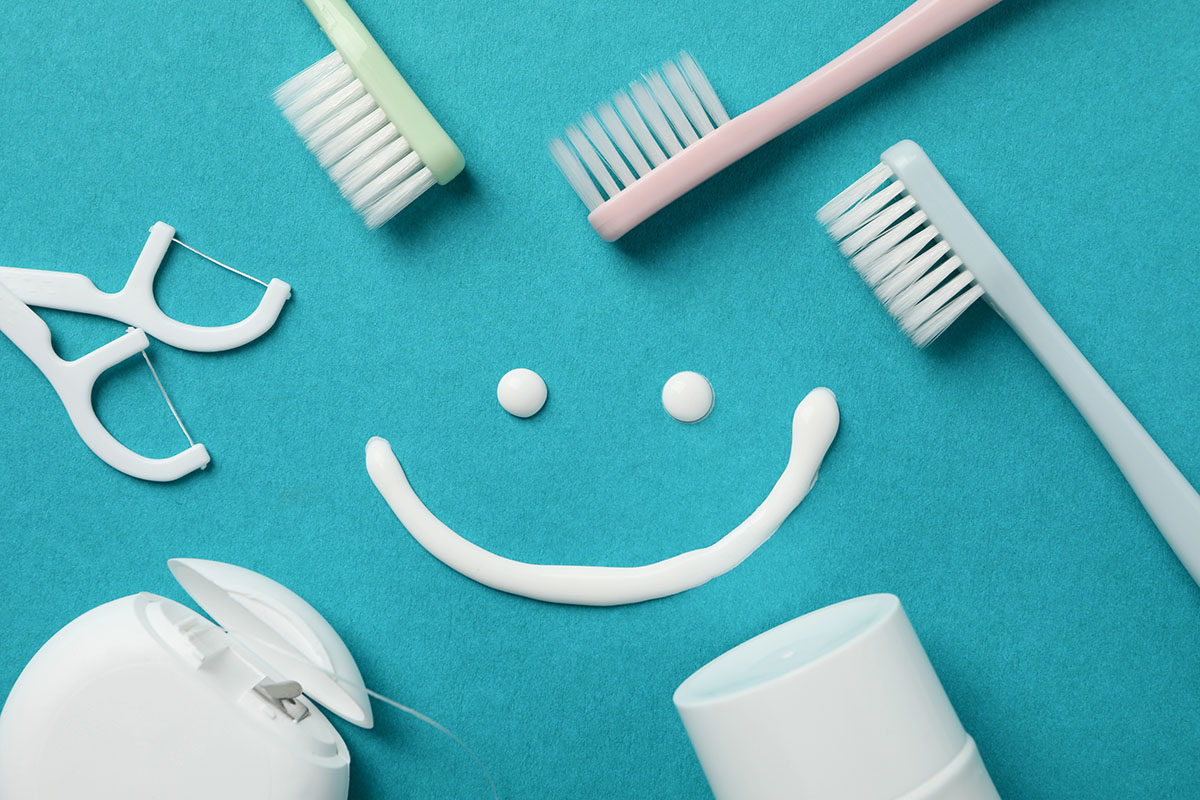 A top-down view shows various dental care tools on turquoise background, with a smile drawn with toothpaste in the middle.