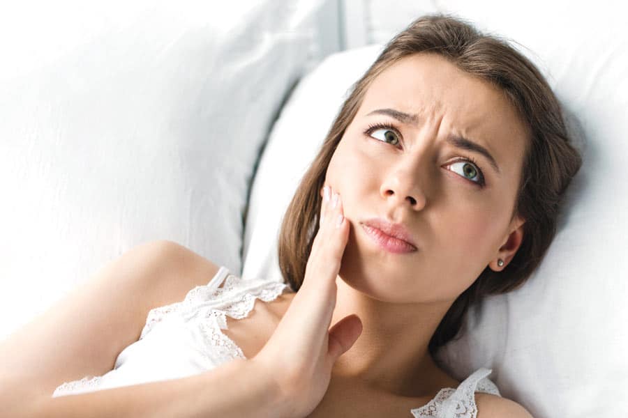 Woman laying on bed with jaw pain